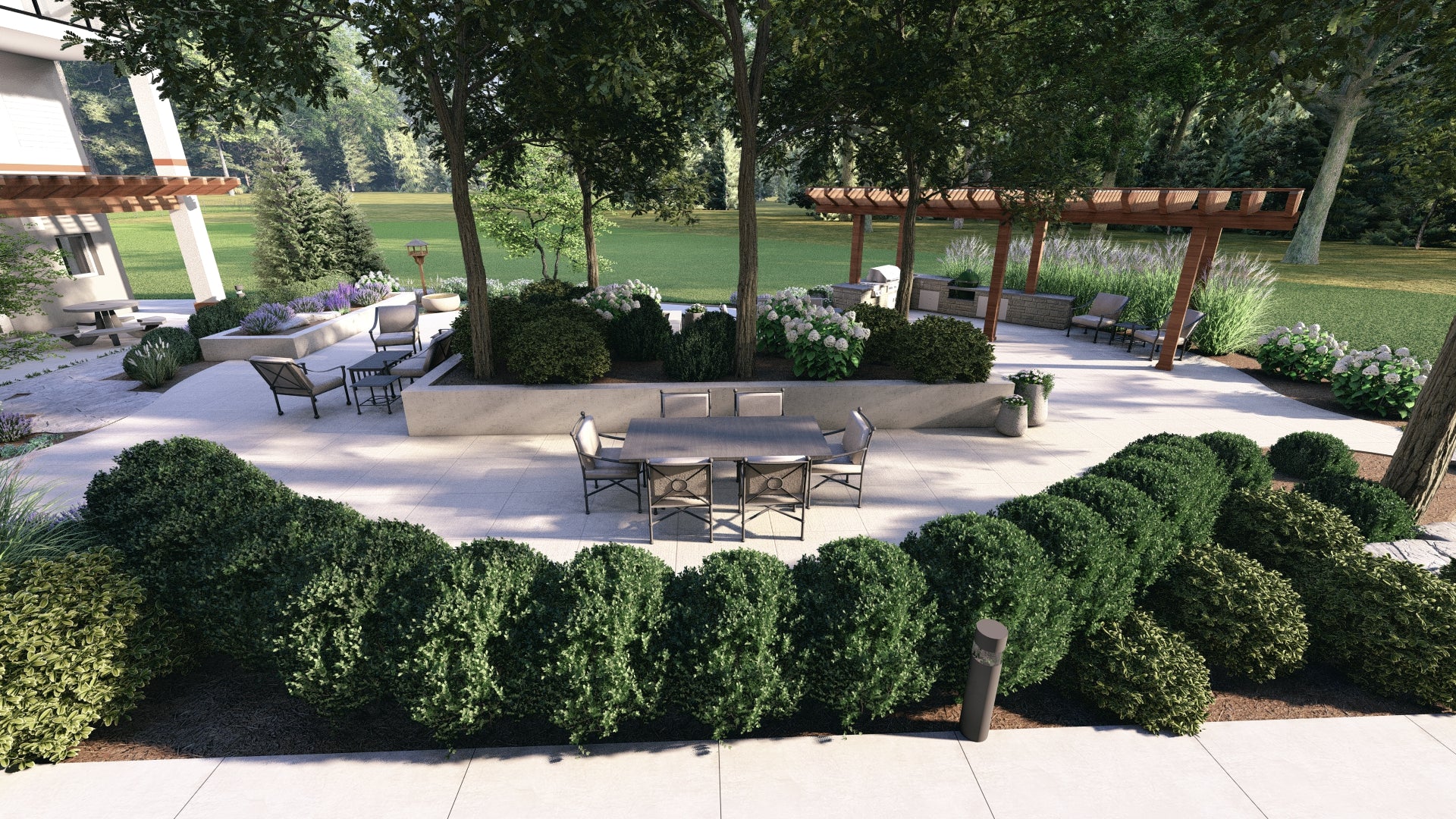 An outdoor patio with a dining table, lounge chairs, and a pergola-covered kitchen area, bordered by bushes and trees.